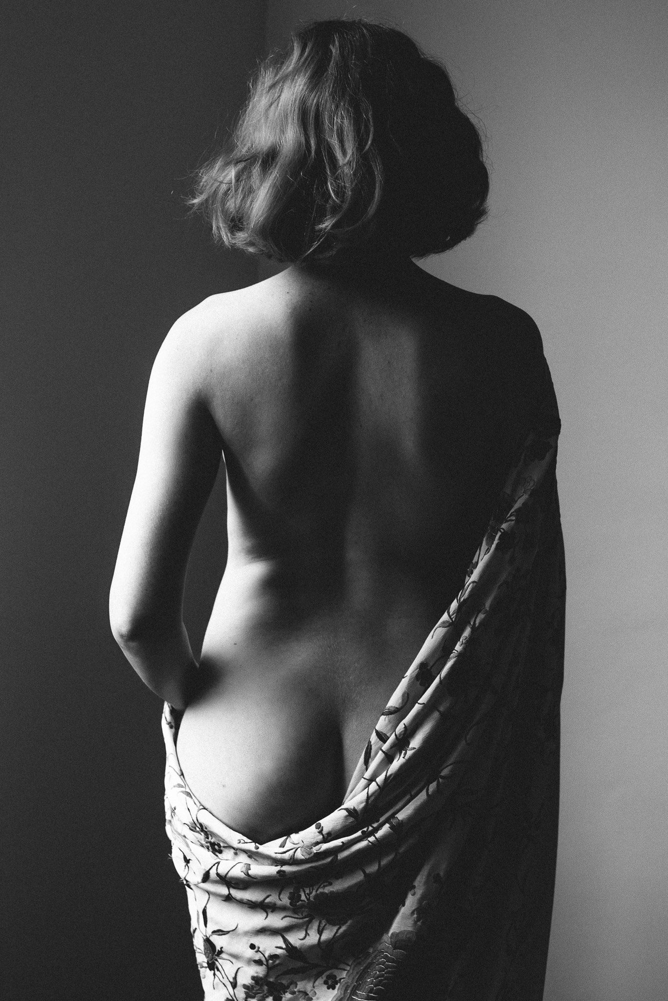 A black and white back view of a woman with a piano shawl obscuring her left buttock.