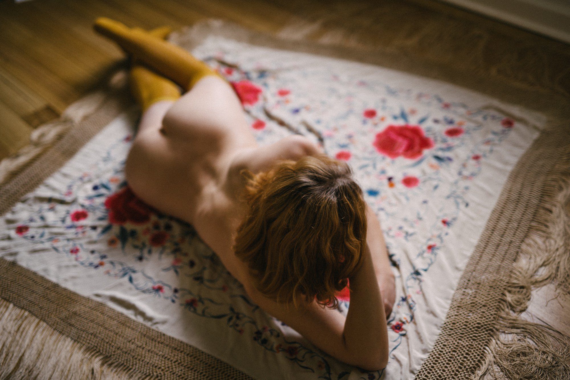 A shallow depth of field photo of a woman lying on a piano shawl, wearing only long orange socks. The focus is on her hair and so her nudity is blurred.