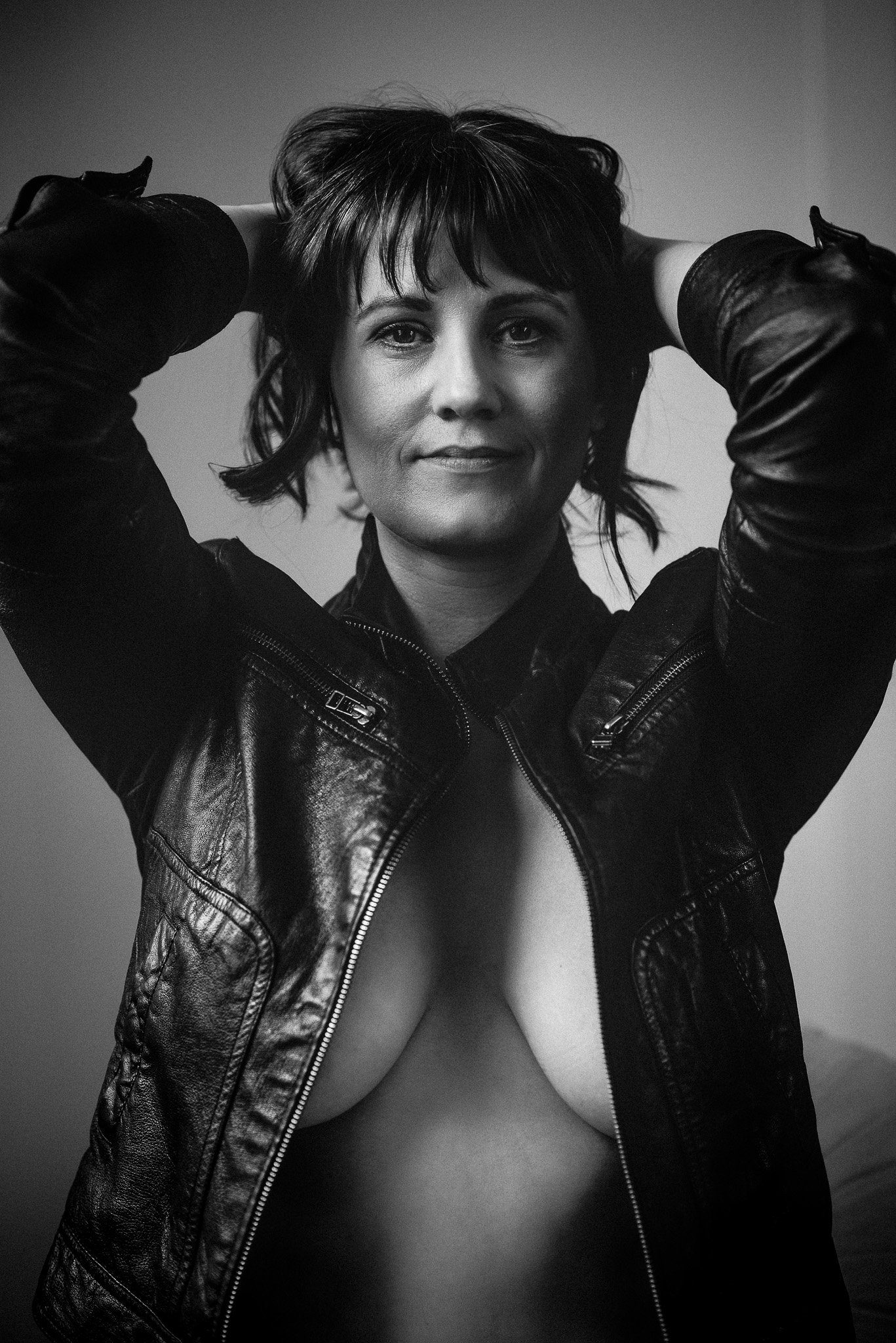 black and white, to the waist, photograph of a lady wearing only a leather jacket open.