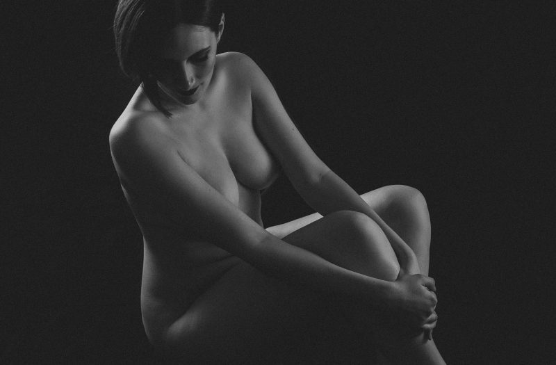 Black and white image of a woman positioned in a way to obscure nipples and genitalia - implied nude.