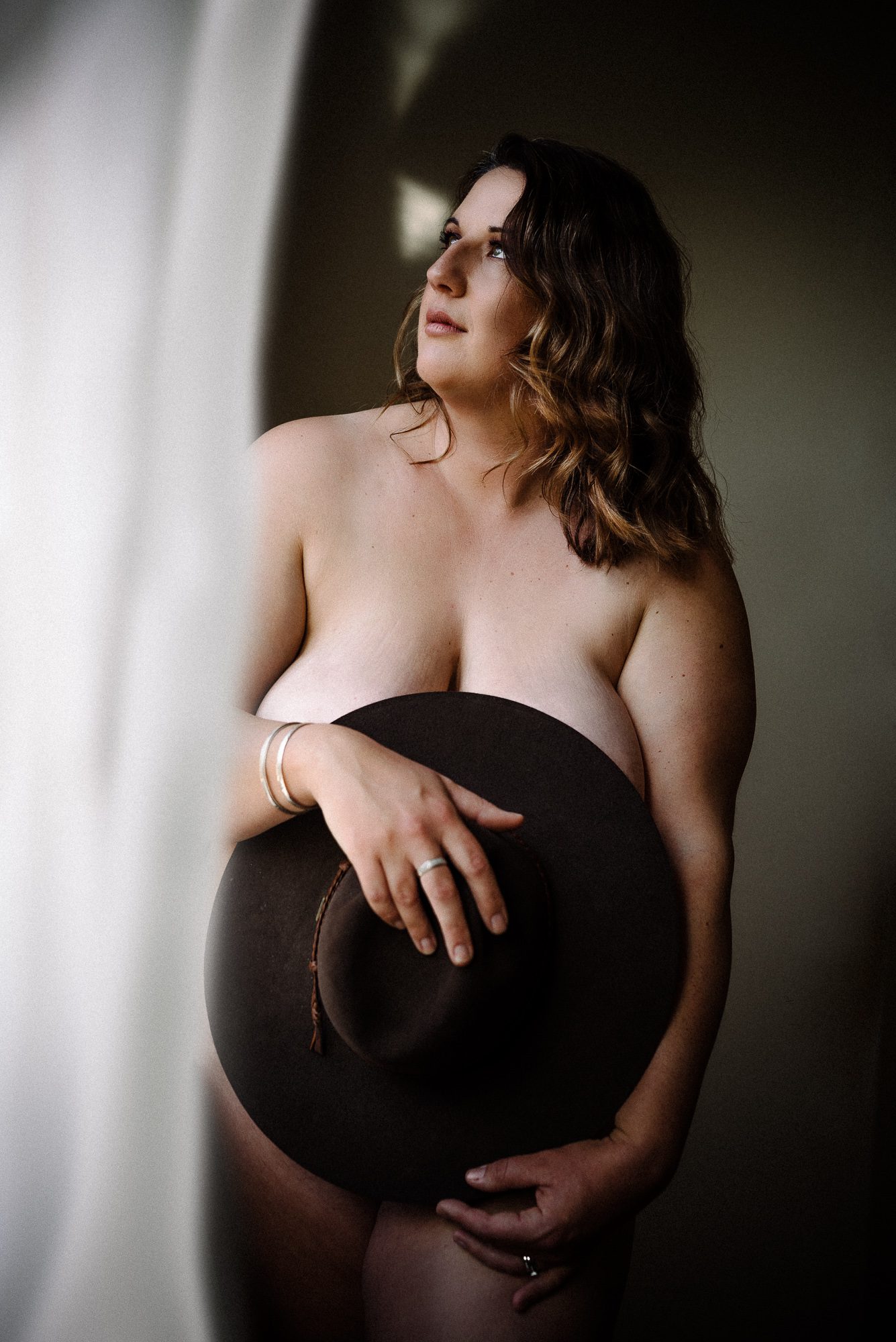 A photograph on a woman holding a cowboy hat in front of her, obscuring her nudity.