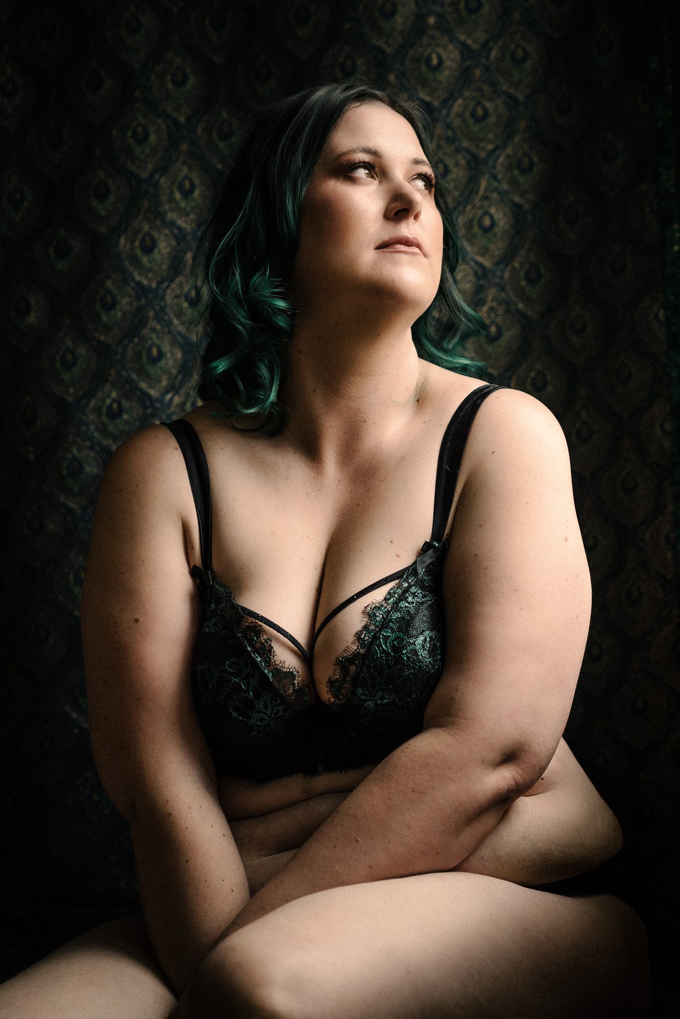 Boudoir photo of a lady with green hair against a peacock backdrop